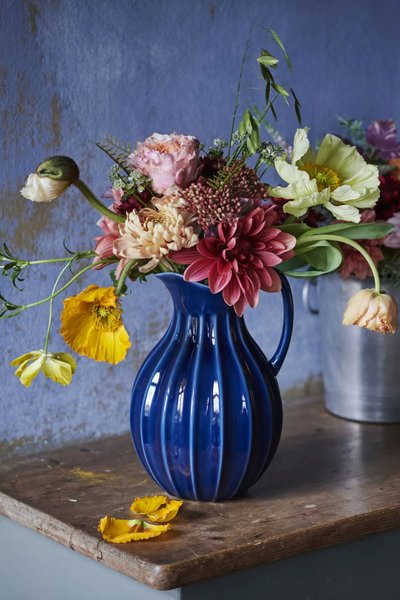 Bouquet de fleurs fraîches aux tons pastel et vifs, arrangé dans un vase bleu cobalt, posé sur une table en bois rustique devant un mur bleu texturé Source - Marie Claire France Pinterest