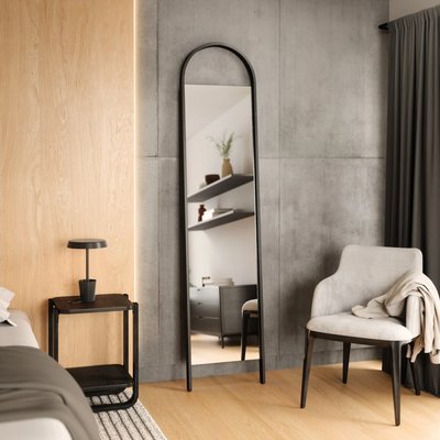 Miroir à adosser au mur Bellwood de Umbra chez Brick – Miroir pleine longueur au cadre noir arrondi, appuyé sur un mur en béton dans une chambre moderne avec accents bois et déco minimaliste.