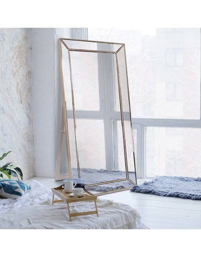 Miroir pleine longueur rectangulaire avec cadre doré élégant de chez Ô Miroir, appuyé contre un mur dans une chambre lumineuse au style bohème.