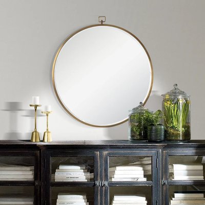 Miroir rond à cadre doré de Lovaco accroché au-dessus d’un buffet noir rustique décoré de chandeliers et de terrariums verts.