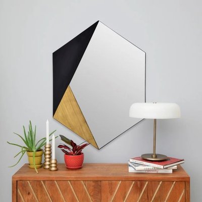Miroir Cad chez Linen Chest – Miroir mural géométrique avec sections en noir, doré et miroir, accroché au-dessus d’une commode en bois décorée de plantes et accessoires modernes.