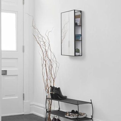 Miroir mural rectangulaire avec rangement intégré en métal noir de chez Kozy, installé dans une entrée minimaliste blanche avec étagère à chaussures.
