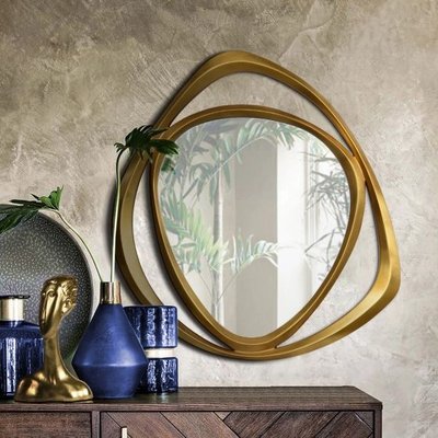 Miroir Goldie chez Linen Chest – Miroir mural rond entouré d’un cadre doré sculptural aux formes fluides, posé au-dessus d’une commode en bois décorée d’accessoires bleu cobalt et dorés.