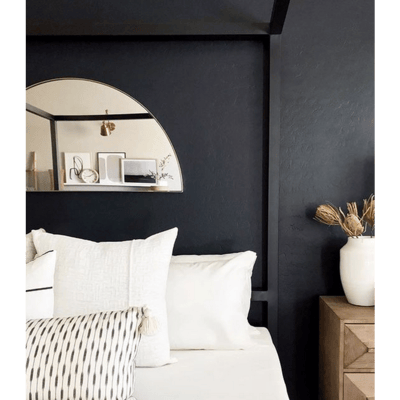 Miroir demi-lune à cadre doré de Lovaco installé au-dessus d’un lit aux tons neutres dans une chambre à mur noir moderne.