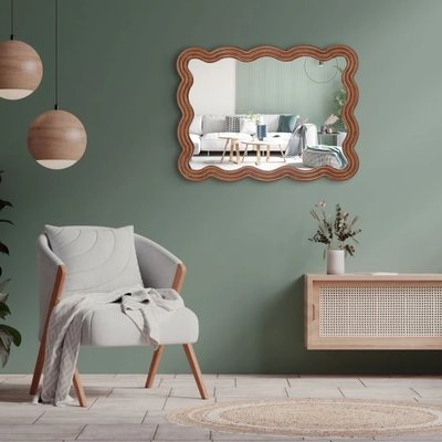 Miroir mural Adria horizontal chez Linen Chest – Miroir décoratif aux contours ondulés en bois, accroché sur un mur vert sauge dans un salon moderne avec fauteuil scandinave et meuble en rotin.