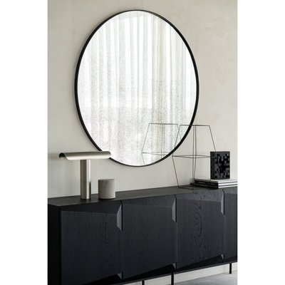 Miroir rond à cadre noir avec effet vieilli de Lovaco, accroché au-dessus d’un buffet noir moderne dans un décor minimaliste.