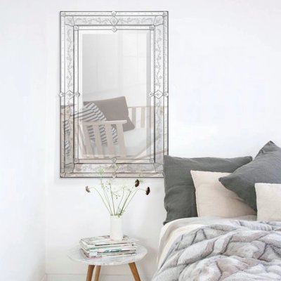 Miroir Vincenzo chez Linen Chest – Miroir rectangulaire au cadre décoratif gravé de motifs floraux et géométriques, accroché au-dessus d’une table d’appoint dans une chambre au style doux et épuré.