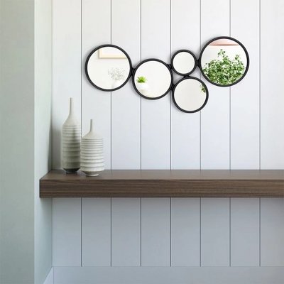 Miroirs ronds Annette noir chez Linen Chest – Ensemble décoratif de cinq miroirs circulaires encadrés de noir, disposés de manière artistique sur un mur à lattes blanches au-dessus d’une tablette en bois moderne.