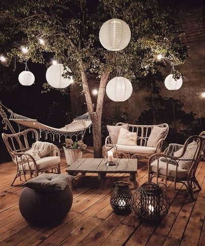 Terrasse bohème en bois éclairée de lanternes et de guirlandes lumineuses Source - Mon Jardin Ma Maison Pinterest Terrasse bohème en bois éclairée de lanternes et de guirlandes lumineuses, avec mobilier en rotin, coussins beiges et hamac suspendu sous un arbre Source - Mon Jardin Ma Maison Pinterest