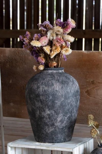 Vase en céramique noir à texture nervurée contenant un bouquet de fleurs séchées dans des tons violets, beige et rosés, posé sur une caisse en bois dans un décor rustique Source - Moss Garden Home Pinterest