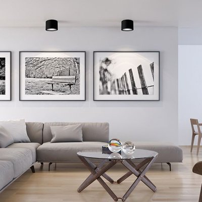 Deux plafonniers cylindriques noirs Mousinni illuminant un salon moderne avec canapé sectionnel gris, table basse ronde en verre et décor minimaliste en noir et blanc – Maison du Luminaire