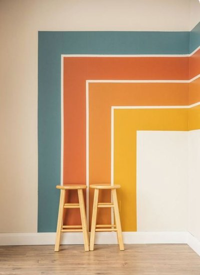 Mur d'angle avec motifs géométriques peints en dégradés de bleu, orange, jaune et beige, avec deux tabourets en bois clair sur un sol en parque Source - Sheila Jensen Pinterest