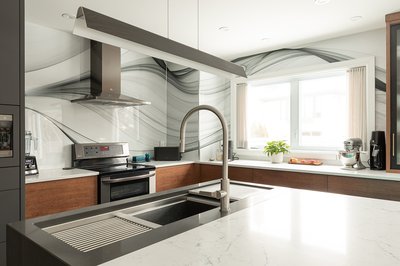 Cuisine moderne avec dosseret en revêtement mural effet marbre aux ondulations gris et noir, armoires en bois foncé, comptoirs en quartz blanc et évier double intégré dans un îlot central, éclairée par une grande fenêtre laissant entrer la lumière naturelle de chez Mur Tendance.