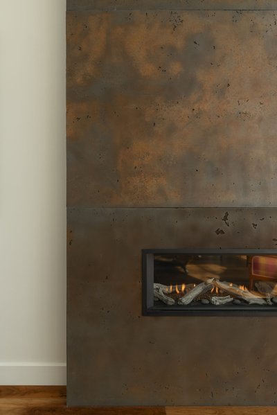 Gros plan sur un revêtement mural effet béton oxydé de style industriel avec foyer au gaz encastré moderne, flammes visibles à travers la vitre, et bûches décoratives imitant le bois naturel, installé dans un salon contemporain avec plancher de bois franc de chez Mur Tendance.