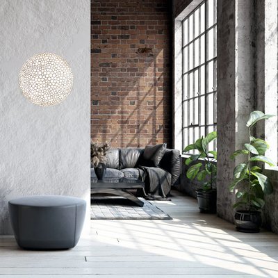 Salon de style loft industriel avec mur en briques apparentes, canapé en cuir noir, grande fenêtre et luminaire mural rond Calipso de chez Luminaires & Cie diffusant une lumière douce