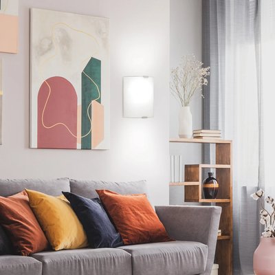 Salon moderne et lumineux avec applique murale blanche au design épuré de chez Luminaires & Cie, canapé gris agrémenté de coussins colorés et œuvre d’art abstraite en arrière-plan