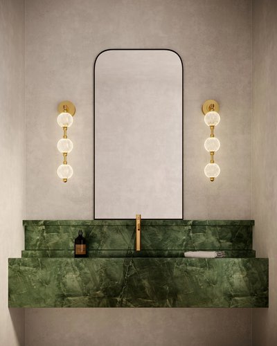 Luminaire mural doré modèle Marni de chez Luminaires & Cie avec trois globes en verre texturé, installé de chaque côté d’un miroir rectangulaire dans une salle de bain au lavabo en marbre vert