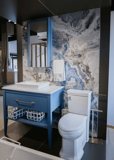 Salle de bain contemporaine avec meuble-lavabo bleu à tiroirs dorés, mur accent marbré aux teintes de bleu et gris, toilette blanche moderne et accessoires dorés dans un décor raffiné de chez Muraluxe