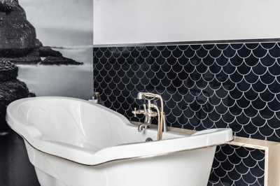Baignoire autoportante blanche au style classique avec robinetterie dorée devant un mur accent en tuiles noires en forme d’écailles de poisson, accompagnée d’une murale artistique en noir et blanc représentant un paysage côtier rocheux de chez Muraluxe