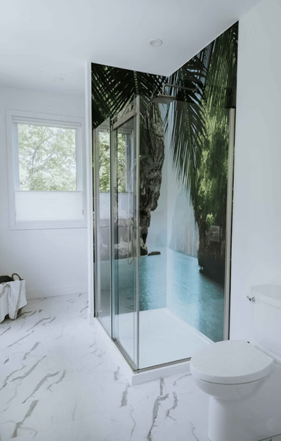 Salle de bain moderne avec douche vitrée ornée d’un revêtement mural représentant un paysage tropical paradisiaque avec palmiers, falaise et eau turquoise, créant une ambiance zen et immersive dans un décor blanc épuré de chez Muraluxe.