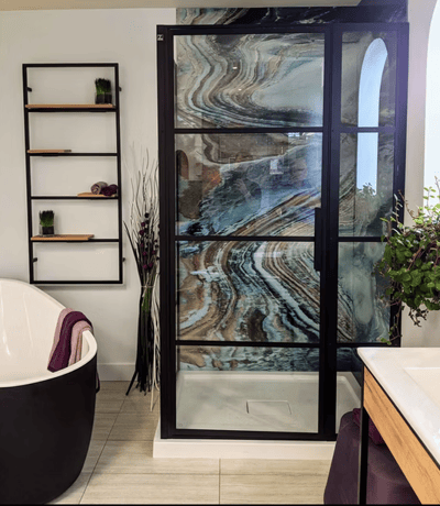 Salle de bain moderne avec douche vitrée encadrée de noir et mur de fond texturé effet marbre fluide aux tons bruns, bleus et beiges, baignoire autoportante blanche à l'extérieur noir, étagère murale minimaliste et accents végétaux décoratifs de chez Muraluxe