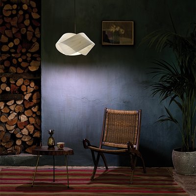 Espace lounge chaleureux avec suspension design blanche Nut de LZF, mise en valeur par un mur vert, un fauteuil en rotin et une table d’appoint rustique – Maison du Luminaire