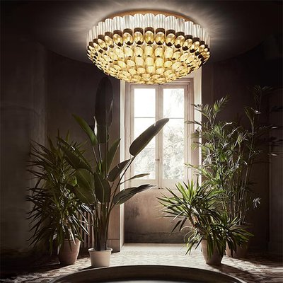 Plafonnier Odeon doré de Slamp, au style glamour et théâtral, éclairant un vestibule végétalisé baigné de lumière naturelle – Maison du Luminaire