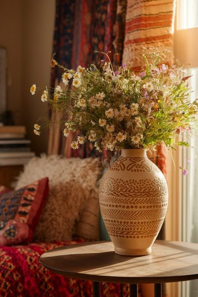 Vase décoratif en terre cuite avec motifs ethniques, garni d'un bouquet champêtre de fleurs séchées, posé sur une table ronde en bois dans un intérieur chaleureux et bohème Source - Ostrali.com - Travel Food Education Australia & Beyond Pinterest