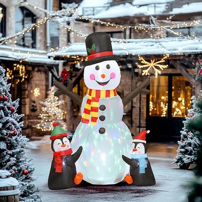 Décoration gonflable de Noël représentant un bonhomme de neige lumineux avec une écharpe rouge et jaune, entouré de deux pingouins portant des bonnets et écharpes colorés, placée au milieu d'une cour décorée avec des guirlandes lumineuses et sapins enneigés - Amazon