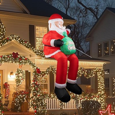 Décoration gonflable du Père Noël assis sur le rebord d'un toit, tenant un sac vert avec l'inscription 'Merry Christmas', entouré de guirlandes lumineuses festives sur une maison décorée pour Noël - Amazon