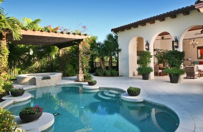 Piscine arrondie avec spa intégré et pergola en bois recouverte de verdure dans une cour méditerranéenne, provenant de Decoist.