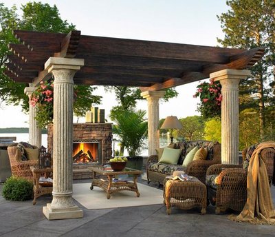 Pergola extérieure en bois sombre avec colonnes classiques et salon en rotin autour d’une cheminée, provenant de Decoist.