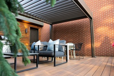 Terrasse en bois avec pergola bioclimatique et mobilier extérieur moderne adossée à un mur de brique rouge de Pergolas Signature