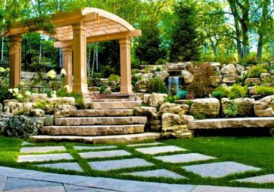 Pergola en bois clair surélevée dans un jardin paysager avec cascade et sentier en pierre, provenant de Decoist.