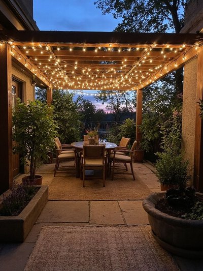Terrasse extérieure avec pergola en bois illuminée de guirlandes lumineuses, table à manger et chaises en rotin dans une ambiance chaleureuse au coucher du soleil Source - Petits Cultivateurs Pinterest