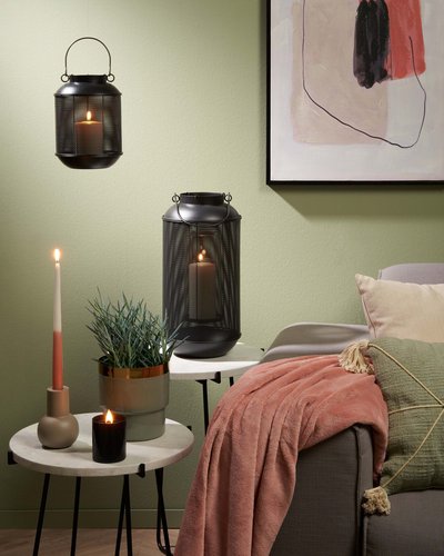 Coin salon décoré avec lanternes noires en métal, bougies allumées, jeté en tissu rose, coussins beiges et verts, plantes décoratives et tables d'appoint en marbre, sur fond de mur vert pâle par Décors Véronneau