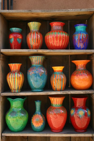 Collection de vases artisanaux colorés aux motifs floraux et géométriques, exposés sur des étagères en bois rustique Source - Rebecca Pavlik Pinterest