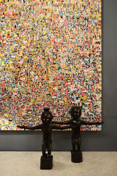 Une grande toile abstraite multicolore Mur d'accent artistique avec une grande toile abstraite multicolore et deux statues tribales sombres placées devant sur un sol en pierre claire