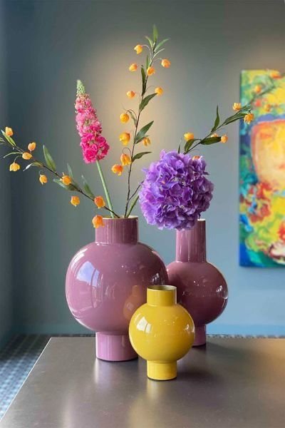 Vases décoratifs modernes rose et jaune disposés sur une table, ornés de fleurs colorées, avec une peinture abstraite en arrière-planm Source - Sofia Pinterest