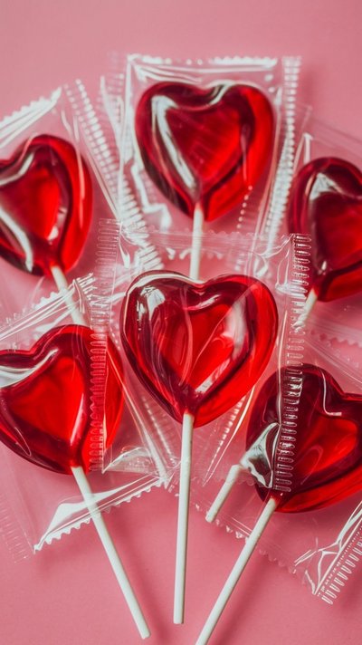 Gros plan de sucettes rouges en forme de cœur, emballées individuellement, sur fond rose - friandises parfaites pour la Saint-Valentin Source - Joyinking Pinterest