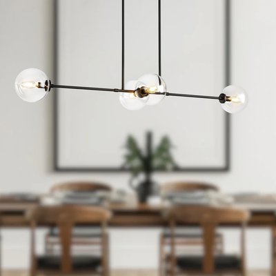 Suspension linéaire Cassia au design épuré de chez Luminaires& Cie, composée de cinq globes en verre transparent montés sur une structure noire minimaliste, suspendue au-dessus d’une table à manger en bois avec chaises assorties, dans une salle à manger contemporaine et lumineuse