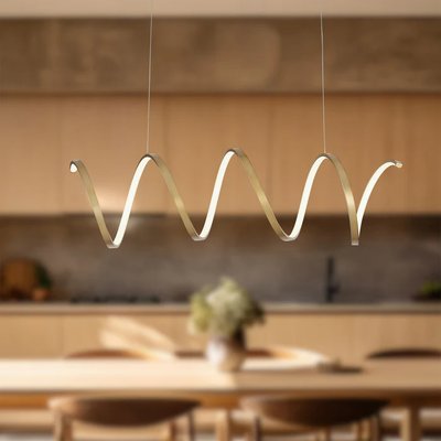 Suspension linéaire Synergy au design ondulé doré de chez Luminaires & Cie, suspendue au-dessus d'une table à manger en bois clair, dans une cuisine moderne au style minimaliste et chaleureux