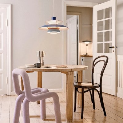 Suspension PH 5 de style scandinave de chez Luminaires & Cie suspendue au-dessus d'une table ronde en bois clair, entourée de chaises dépareillées dont une chaise moderne en tissu mauve et une chaise classique noire, dans une salle à manger lumineuse à l’ambiance douce et minimaliste