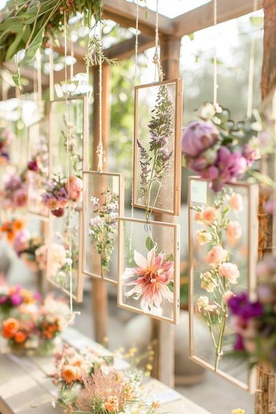 Fleurs pressées suspendues entre des cadres de verre accrochés à une structure en bois, dans une ambiance lumineuse et romantique Source - Wendy Barnoski Pinterest