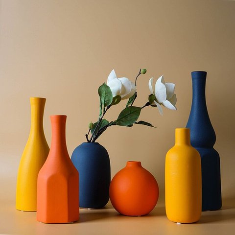 Collection de vases décoratifs en céramique aux teintes orange, jaune et bleu marine, avec fleurs blanches artificielles, sur fond beige - Benigna Nunes Pinterest