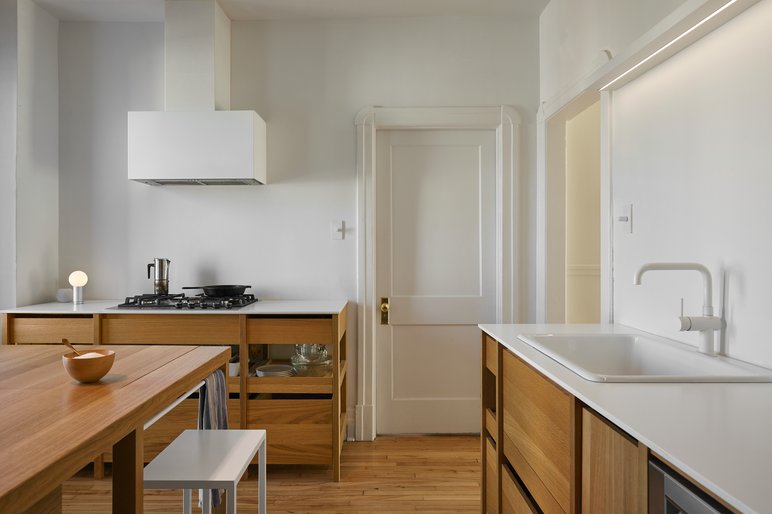 Cuisine moderne et minimaliste avec des armoires en bois clair, comptoirs blancs, évier intégré avec robinet blanc, cuisinière à gaz, hotte murale blanche et table en bois avec un tabouret blanc. Cuisine moderne et minimaliste avec des armoires en bois clair, comptoirs blancs, évier intégré avec robinet blanc, cuisinière à gaz, hotte murale blanche et table en bois avec un tabouret blanc.