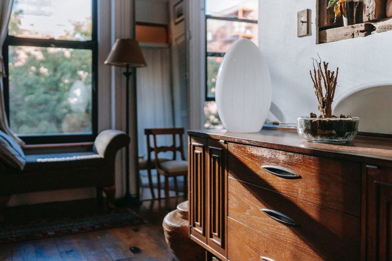 Buffet en Bois Vintage de Avec une Lampe Décorative Blanche de Chez Meublétout Buffet en bois vintage avec une lampe décorative blanche et une plante, dans un salon lumineux au style rétro avec vue sur l'extérieur de Chez Meublétout