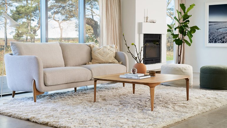 Salon Lumineux avec Canapé Beige Moderne Salon lumineux avec canapé beige moderne, table basse en bois, tapis moelleux et accents de décoration naturels, entouré de grandes fenêtres avec vue sur la nature.