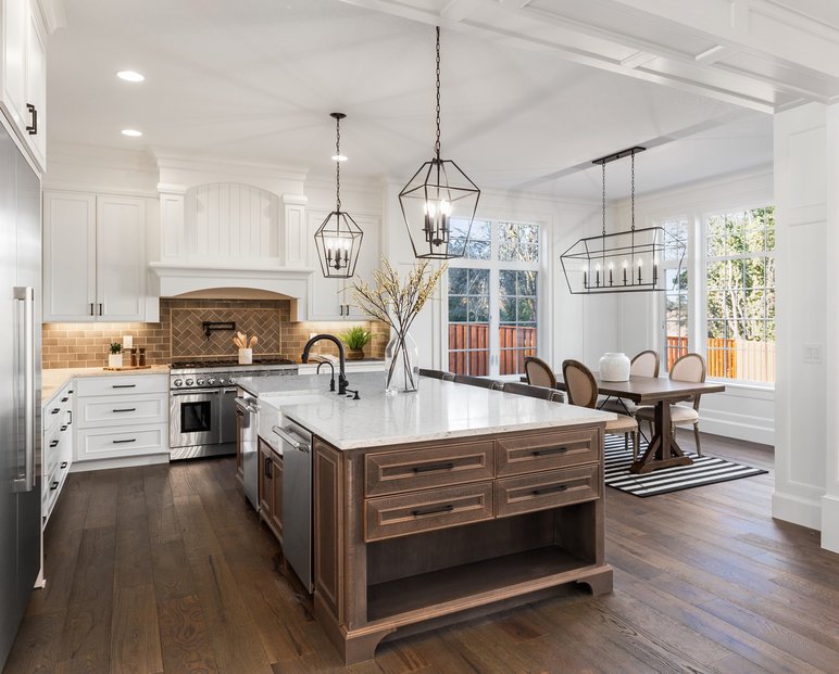 Cuisine haut de gamme moderne avec îlot central en bois foncé, armoires blanches et luminaires suspendus – réalisation par RenoVilla