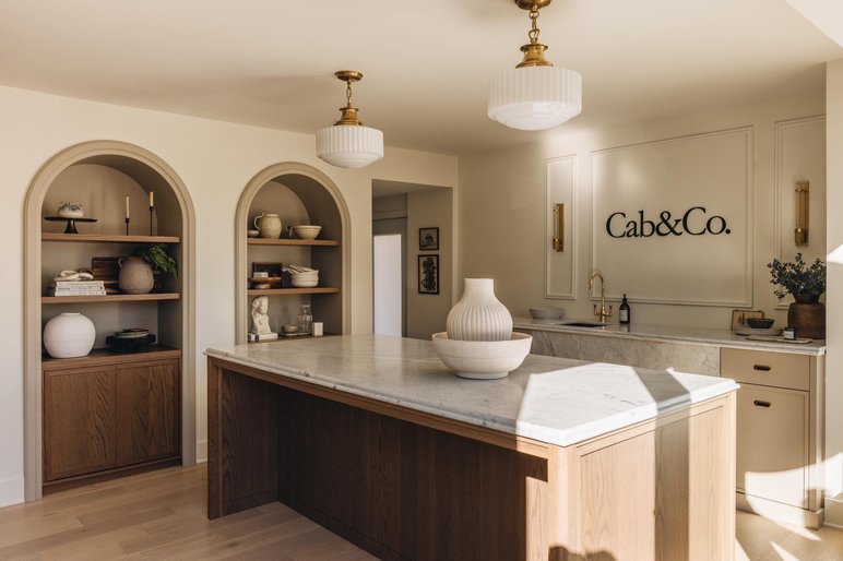 Cuisine moderne au design raffiné par Cab&Co. Cuisine moderne au design raffiné par Cab&Co., avec îlot en marbre, armoires en bois et étagères encastrées décorées d’objets artisanaux.